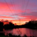 Photo of a spectacular pink, purple and orange sunset over the lake, with pylon silhouetted