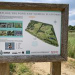 Photo of an information board encouraging visitors to explore the pond and viewing platforms.