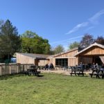 Photo taken of the area behind the cafe and visitor centre. Lots of wooden tables outside and people enjoying the sunshine.